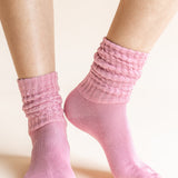 A pair of light pink ribbed scrunch socks worn on a person's feet, shown against a solid pale beige background.
