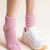 A close-up of a person's feet wearing a pair of light pink ribbed crew socks and white sneakers against a solid light beige background.
