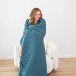 Standing and smiling model wrapped in the Kyte Quilt Blanket in Atlantic 2.5 TOG