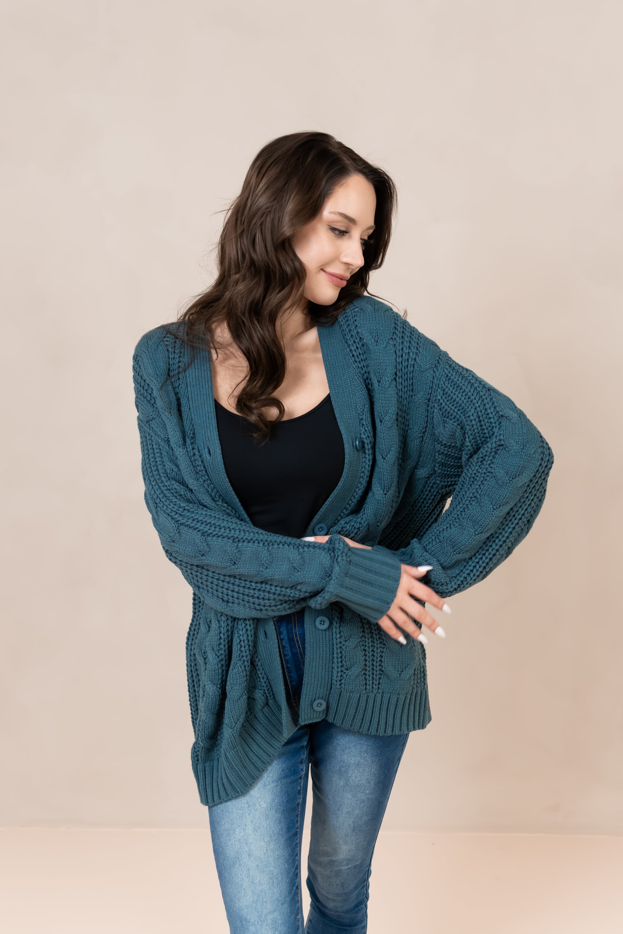 Model looking to the side with unbuttoned Chunky Cable Knit Cardigan in Atlantic paired with jeans