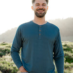 Smiling model in front of a grassy background while wearing a Kyte Long Sleeve Henley in Atlantic