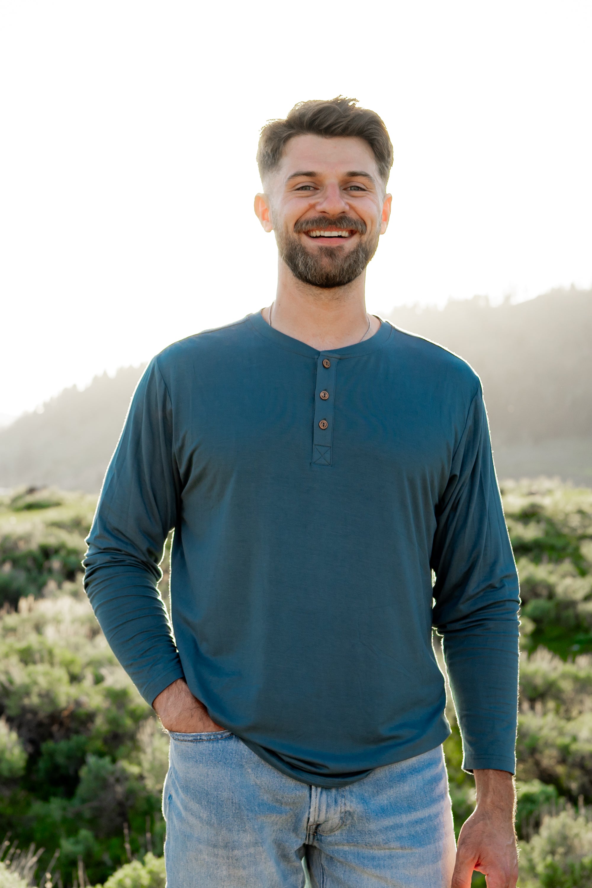 Smiling model in front of a grassy background while wearing a Kyte Long Sleeve Henley in Atlantic