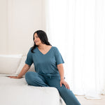 Model sitting on a bed wearing matching V Neck and  Lounge pants in Atlantic