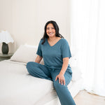 Smiling model sitting on side of bed while wearing Women's Lounge Pants in Atlantic