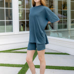 Woman wearing a blue outfit standing in a modern indoor setting with large windows.