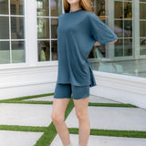 Woman wearing a blue outfit standing in a modern indoor setting with large windows.