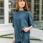 Woman wearing a teal outfit standing in front of a glass door. ::: Model is 5'6" wearing size S ///