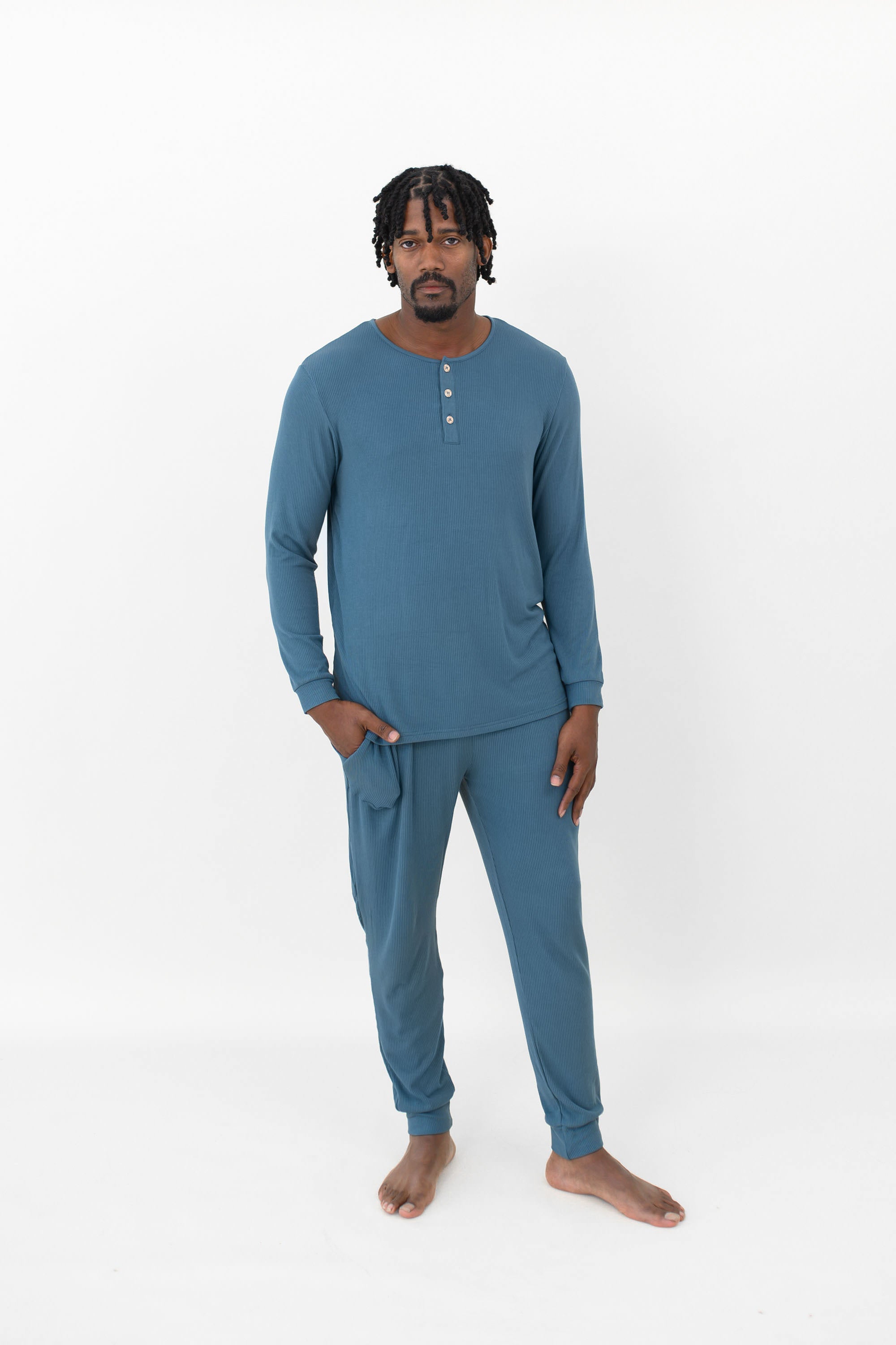 Male model standing wearing the Men's Ribbed Henley Set in Atlantic with one hand in the pants pocket in front of a white back drop