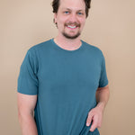 Smiling model wearing Men's Crew Neck Tee in Atlantic with hands at bottom hem