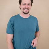 Smiling model wearing Men's Crew Neck Tee in Atlantic with hands at bottom hem