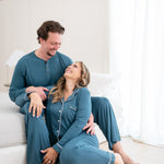 Man wearing the Kyte Men's Henley Top in Atlantic while smiling down at woman in matching Long Sleeve Woman' Pajama Set