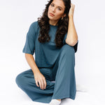 Female model sitting on the floor wearing the Women's Short Sleeve Tee in Atlantic with matching wide leg pants