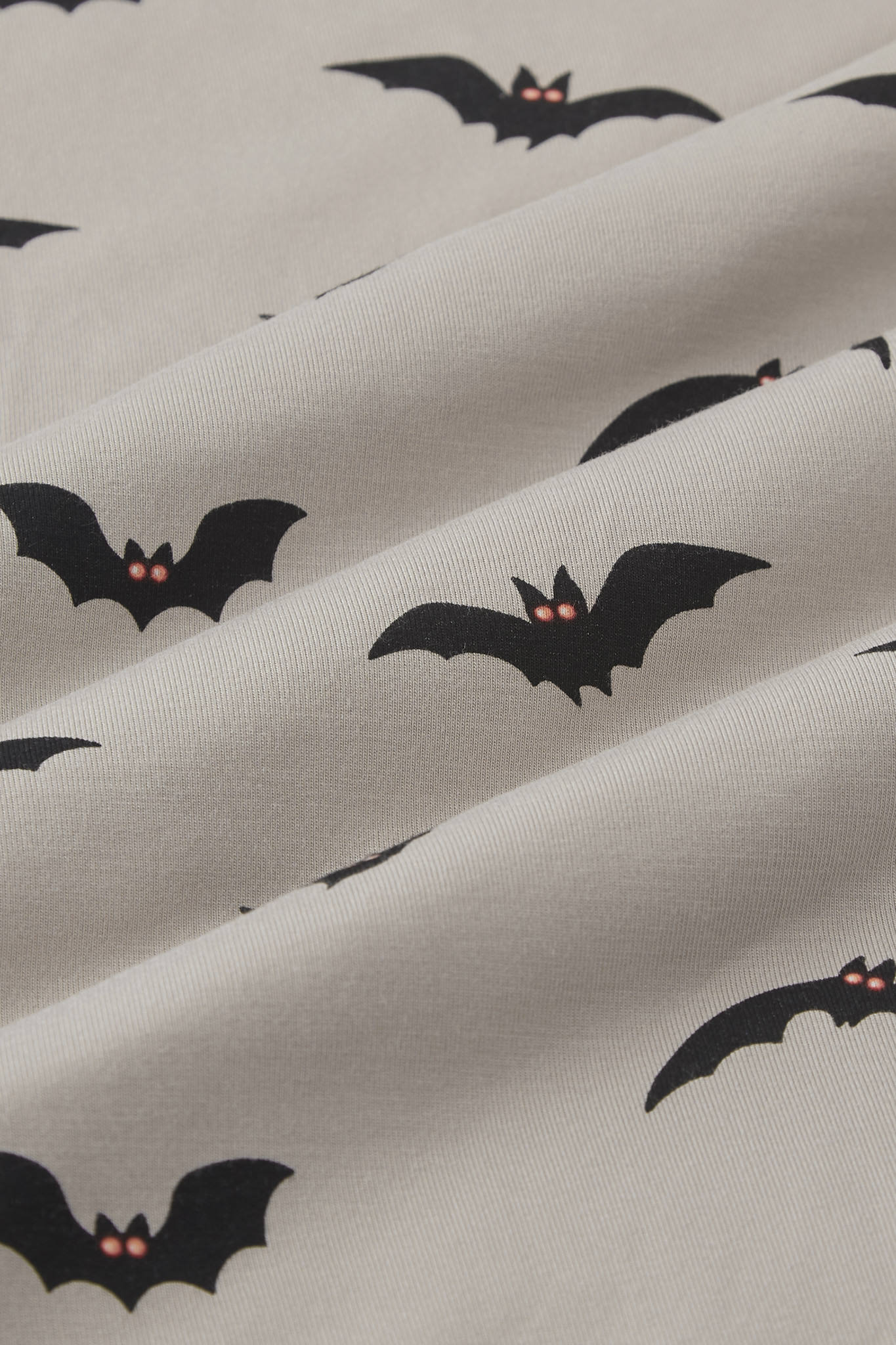 An all-over print featuring the silhouettes of various flying bats with orange eyes over a light tan background color called Khaki. ---1605 1