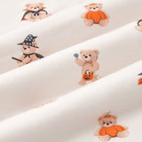 A repeating, all-over print featuring: a light brown teddy bear with white fangs, wearing a black and orange vampire cape and a purple bow around its neck;a teddy bear holding a lollipop in one hand and a jack o’ lantern basket with candy falling out in the other;a teddy bear sitting inside an orange pumpkin and wearing the pumpkin top on its head; a teddy bear riding a black and orange broom,wearing a starry black witch’s hat and black cape around its neck, over an off-white background color called Vanilla