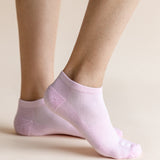 A close-up of a person's feet wearing light pink low-cut ankle socks against a solid beige background.