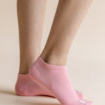 A close-up of a person's feet wearing light pink low-cut ribbed ankle socks against a solid pale beige background.