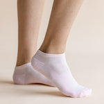 A pair of light pink low-cut ankle socks worn on a person's feet, shown against a solid, warm beige background.