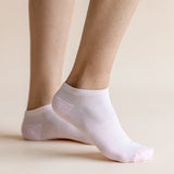 A pair of light pink low-cut ankle socks worn on a person's feet, shown against a solid, warm beige background.
