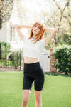 Model standing in a yard with arms up wearing the Kyte Bamboo Flex High Rise Biker Short in Midnight paired with the Bamboo Flex Cloud Baby Tee ::: Model is 5'6" wearing size XS ///

