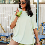 Woman modeling the Biker Short Set in Basil outfit drinking from a straw in an outdoor setting ::: Model is 5' wearing size XS ///