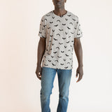Modal posing in Men's Crew Neck Tee in Bats print over blue jeans on a beige background
