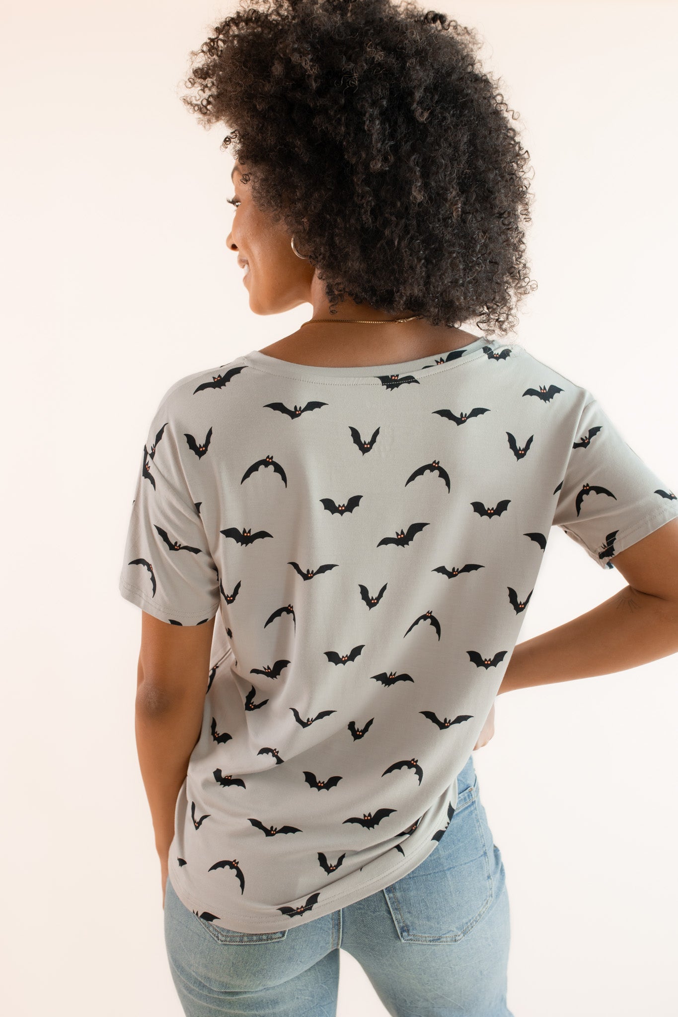 Back side of Modal wearing Women's Oversized V-Neck Tee in Bats print over light blue jeans on a beige background