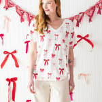 Model standing in front of a white wall decorated with bows and wearing the Bamboo Women's Relaxed Fit V-Neck in Big Love Bow