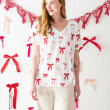 Model standing in front of a white wall decorated with bows and wearing the Bamboo Women's Relaxed Fit V-Neck in Big Love Bow