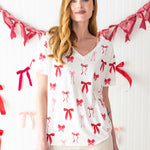 Woman standing in front of a streamer of bows while modeling the Bamboo Women's Relaxed Fit V-Neck in Big Love Bow