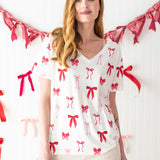 Woman standing in front of a streamer of bows while modeling the Bamboo Women's Relaxed Fit V-Neck in Big Love Bow