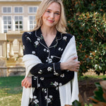 Woman outside soft smiling wearing a long sleeve pajama set in midnight magnolia with a cardigan draped over her arms.
---1605 1