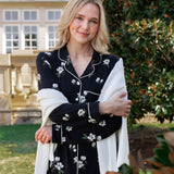 Woman outside soft smiling wearing a long sleeve pajama set in midnight magnolia with a cardigan draped over her arms.
---1605 1