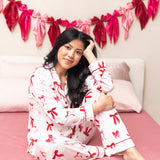 Woman sitting on a pink bed while wearing the Bamboo Long-Sleeved Women's Pajama Set in Big Love Bow