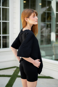 Woman wearing a black biker short outfit standing outdoors near a building.