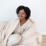 Close up of smiling model curled in a Blanket in Bisque 2.5 and matching Long Sleeve Pajama Set