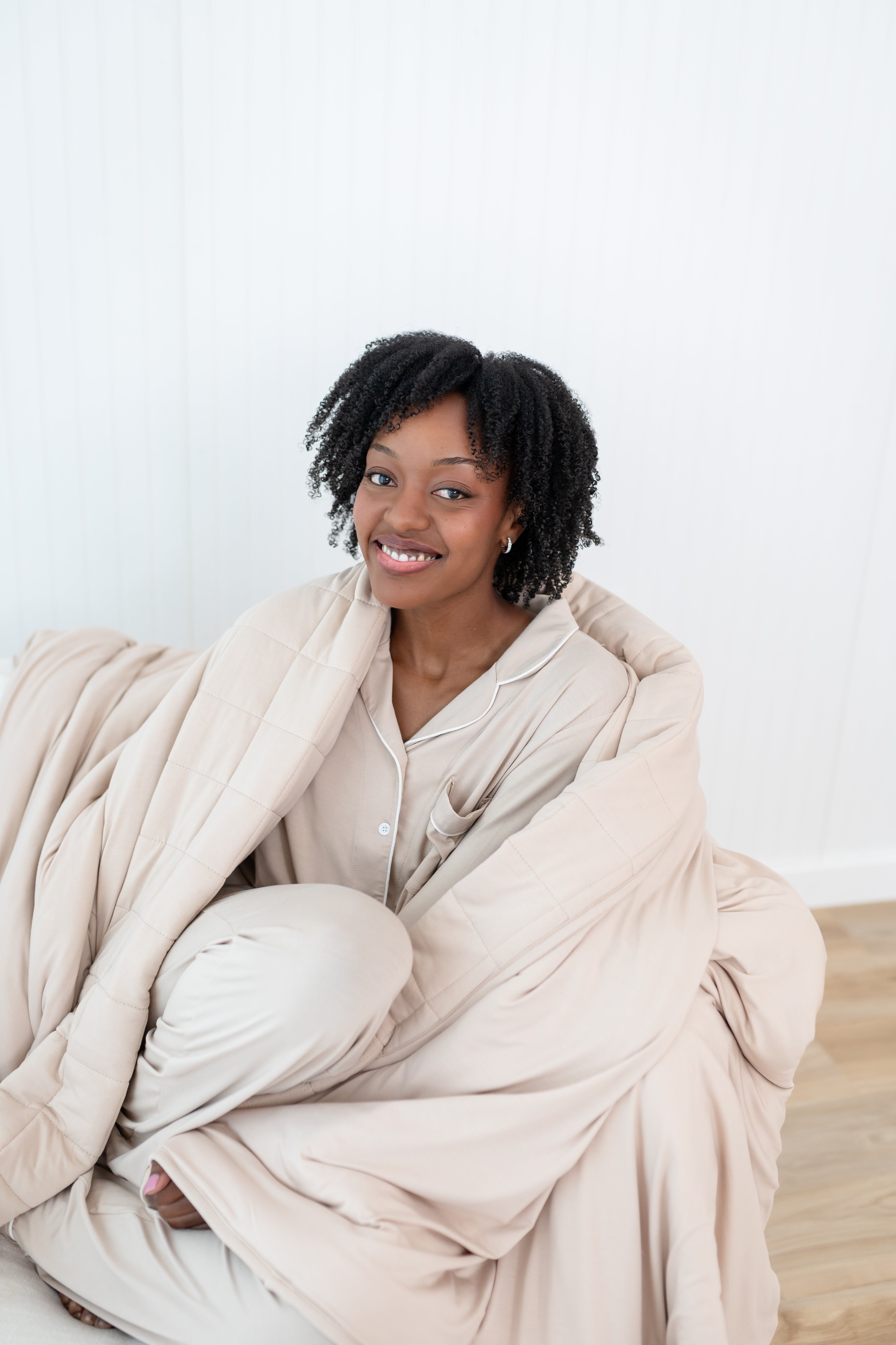 Close up of smiling model curled in a Blanket in Bisque 2.5 and matching Long Sleeve Pajama Set