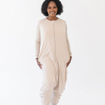 Smiling model standing in a white room while wearing the Kyte Adult Sleep Bag Walker in Bisque
