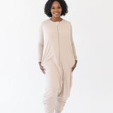 Smiling model standing in a white room while wearing the Kyte Adult Sleep Bag Walker in Bisque