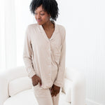Woman in beige pajamas sitting on a white chair in a bright room.
