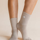 A close-up of a person's feet and lower legs wearing light gray ribbed crew socks against a warm beige studio background.