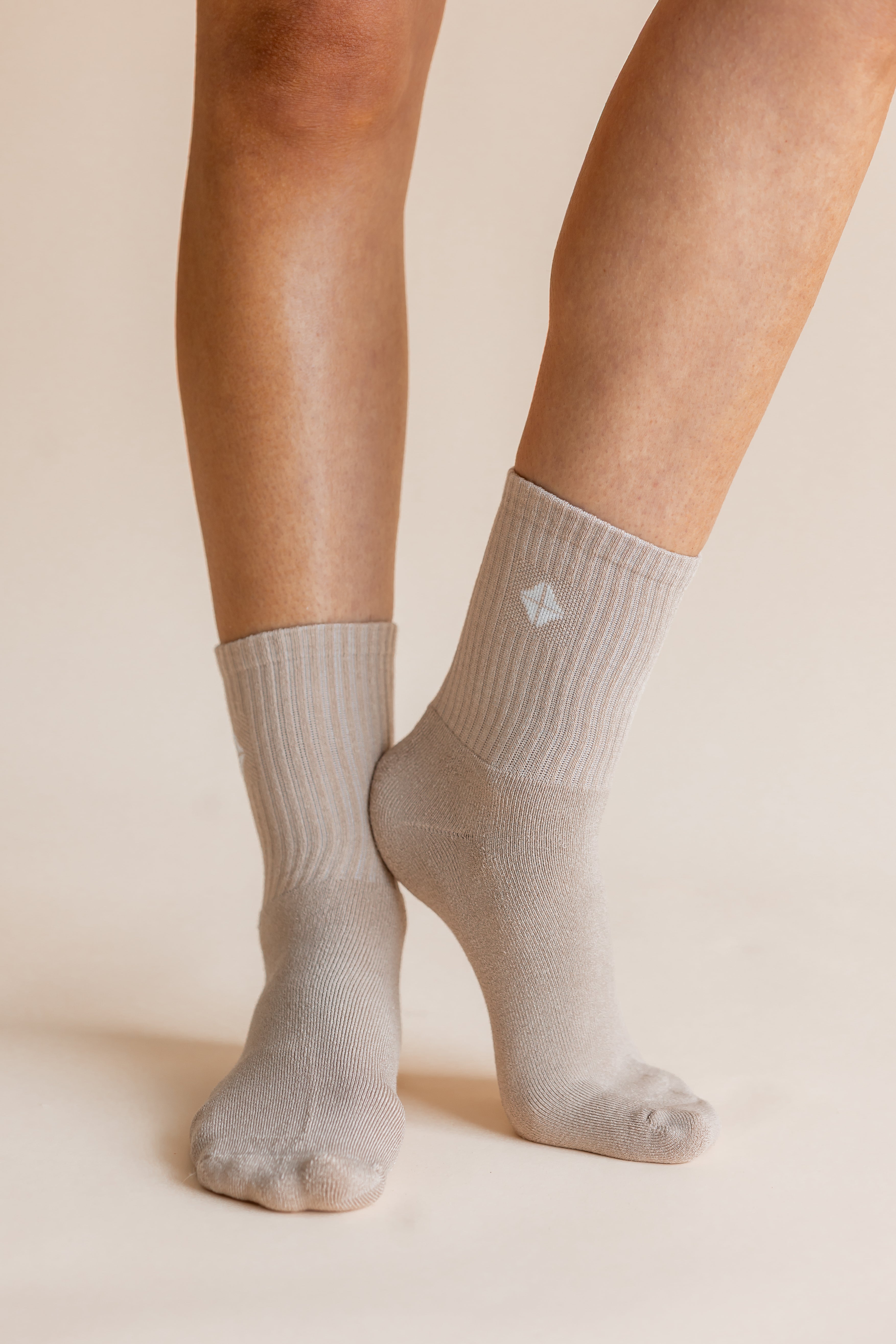 A close-up of a person's feet and lower legs wearing light gray ribbed crew socks against a warm beige studio background.