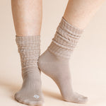 A close-up of a person's feet wearing light taupe ribbed crew socks against a solid beige background.
