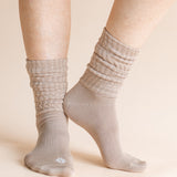 A close-up of a person's feet wearing light taupe ribbed crew socks against a solid beige background.