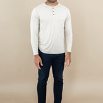 Model standing in tan rom while wearing the Kyte Men's Long Sleeve Henley in Bisque paired with dark-wash jeans