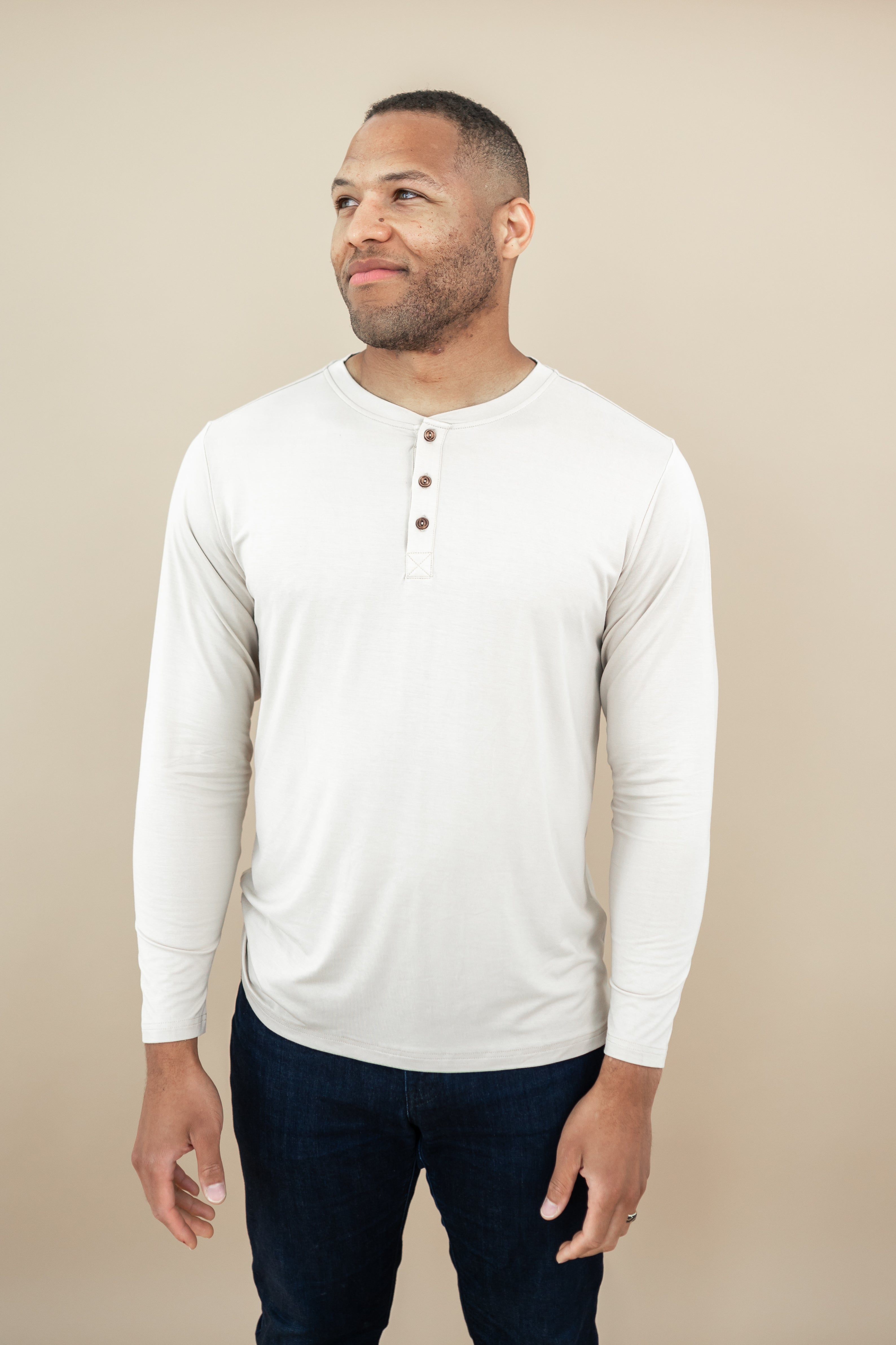 Smiling model looking to the side while wearing the Men's Long Sleeve Henley Tee in Bisque
