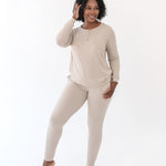 Smiling female standing with one hand in her hair and the other hand in the pants pocket of the Women’s Ribbed Henley Set in Bisque