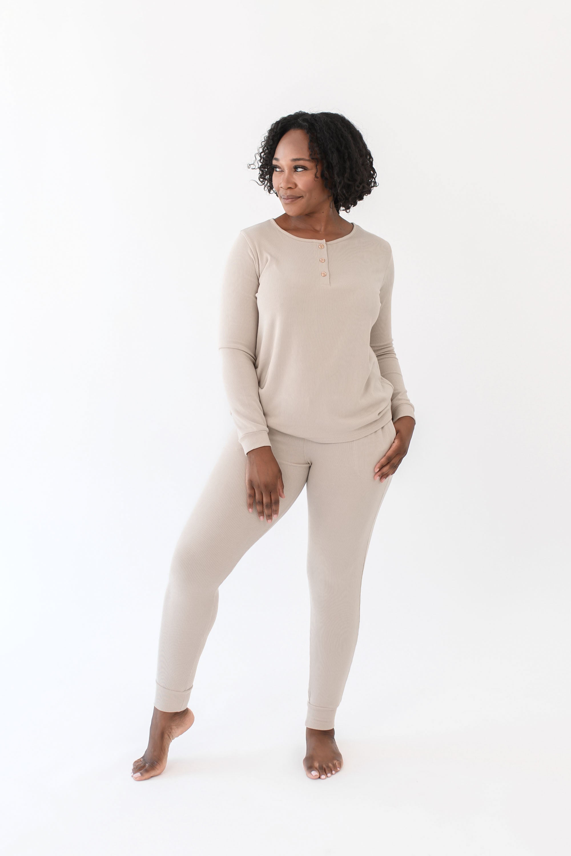 Female model standing looking off to the side wearing the Women’s Ribbed Henley Set in Bisque with one hand in the jogger pants pocket