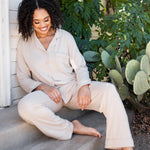 Smiling female sitting on concrete steps wearing the Long-Sleeved Women's Pajama Set in Bisque with Bisque Trim