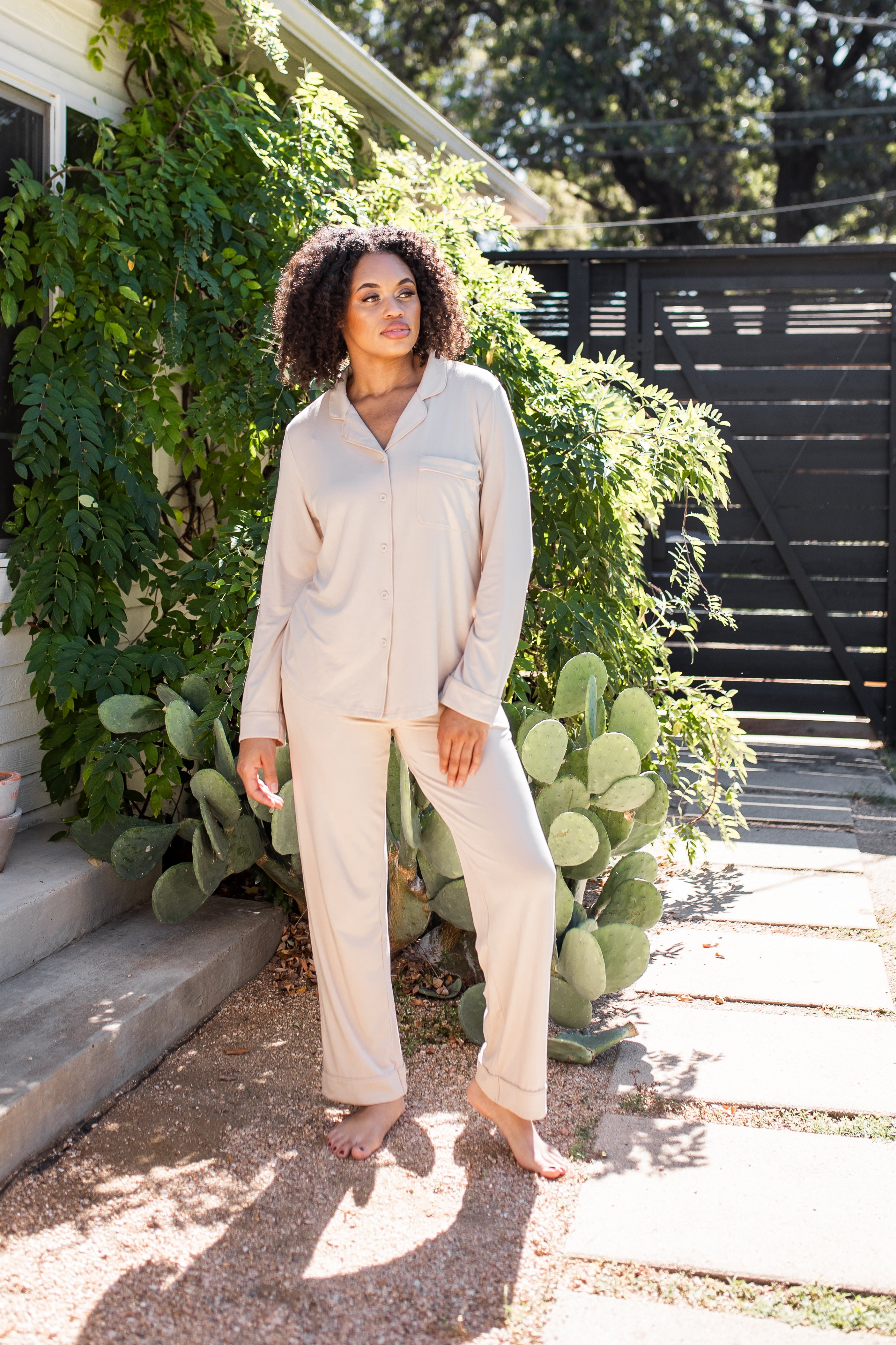 Female standing outside in front of greenery wearing the Long-Sleeved Women's Pajama Set in Bisque with Bisque Trim