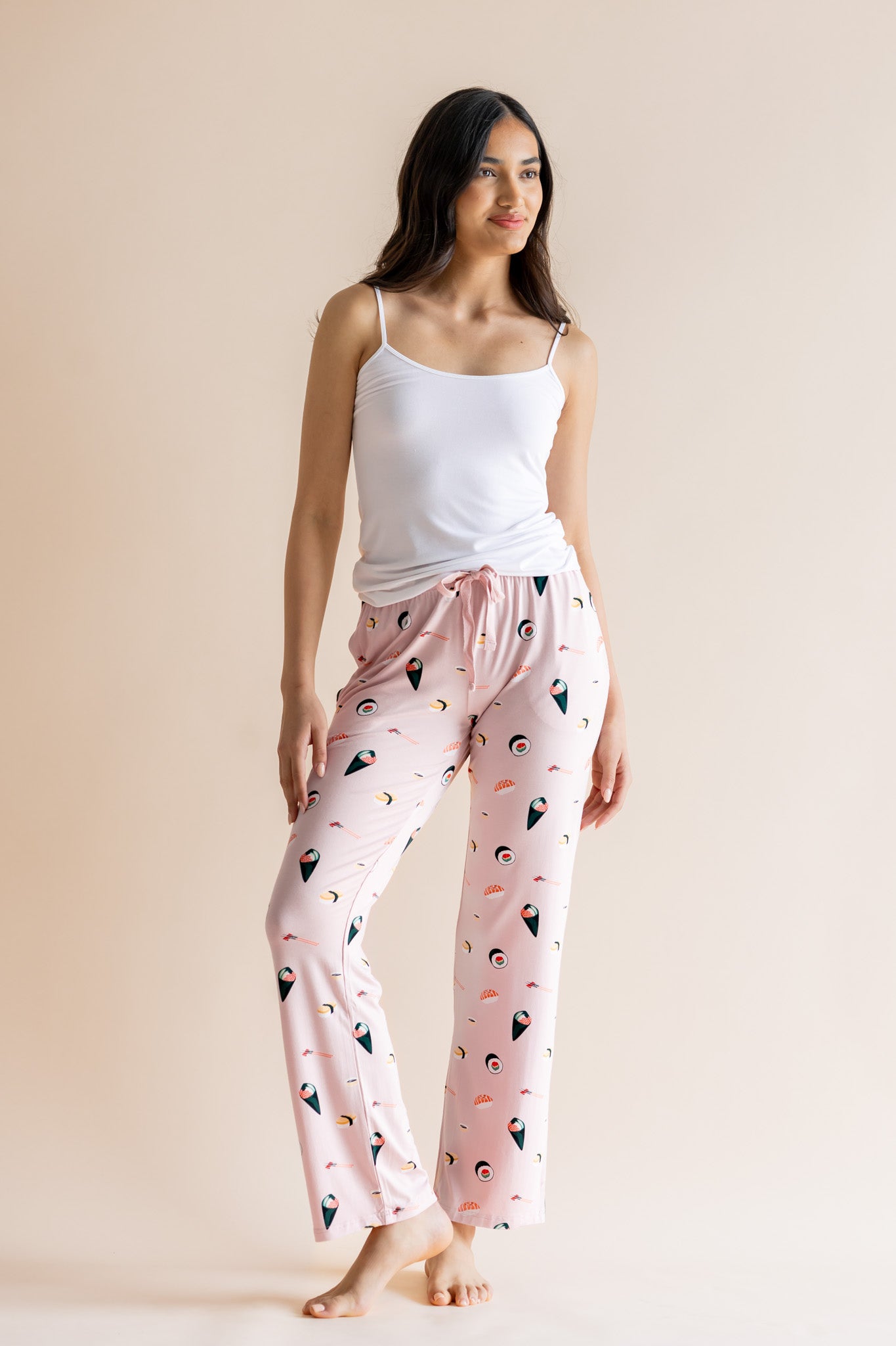 Model wearing pink Women's Lounge Pants in Sushi print under white camisole on a beige background 